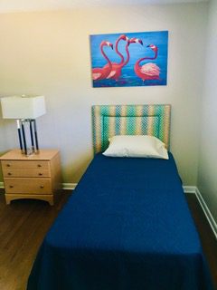 A bed room with a blue headboard and a flamingo painting on the wall.