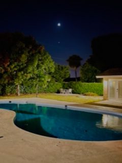 A pool with a bench and gazebo in the background.